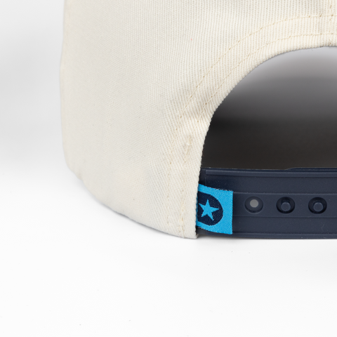 closeup of adjustable strap on back of cream and navy hat showing label with "D" star logo