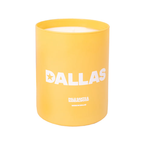 Yellow candle with white text "DALLAS PALO SANTO & SANDALWOOD MAD IN DALLAS"
